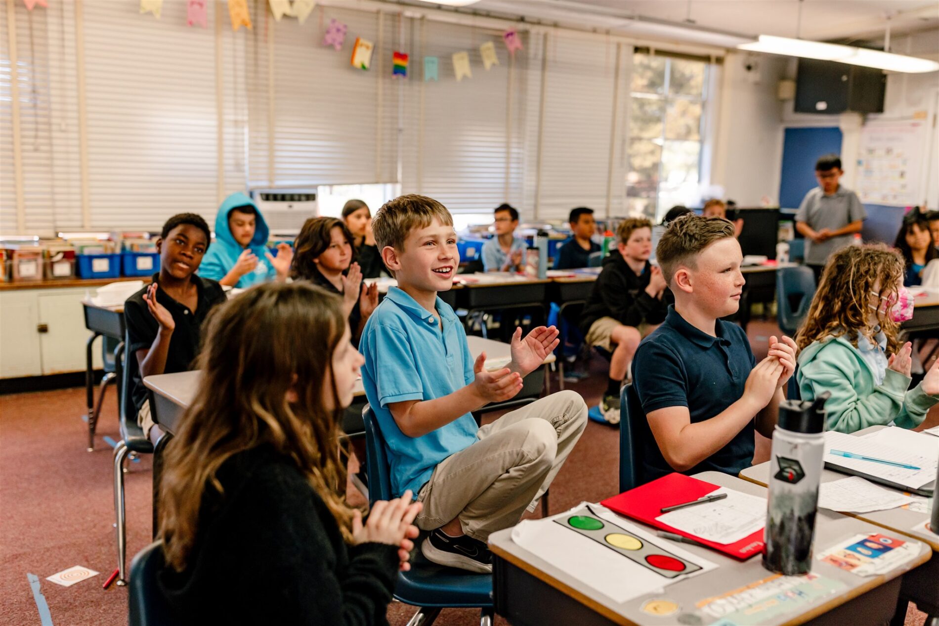 Kavod students sitting at their desks facing the Teacher, clapping along and engaged in a lesson.