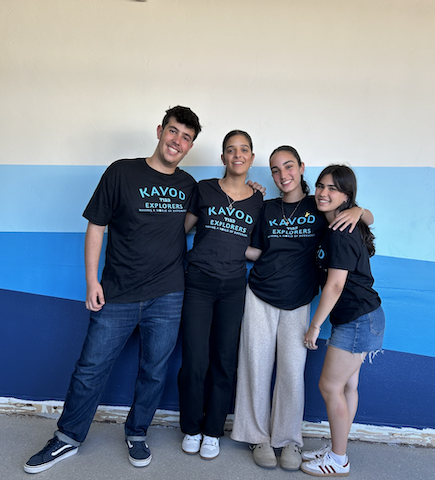 Four Kavod Shinshinim Interns wearing matching Kavod Explorers shirts smile and pose for a photo with their arms around each other.