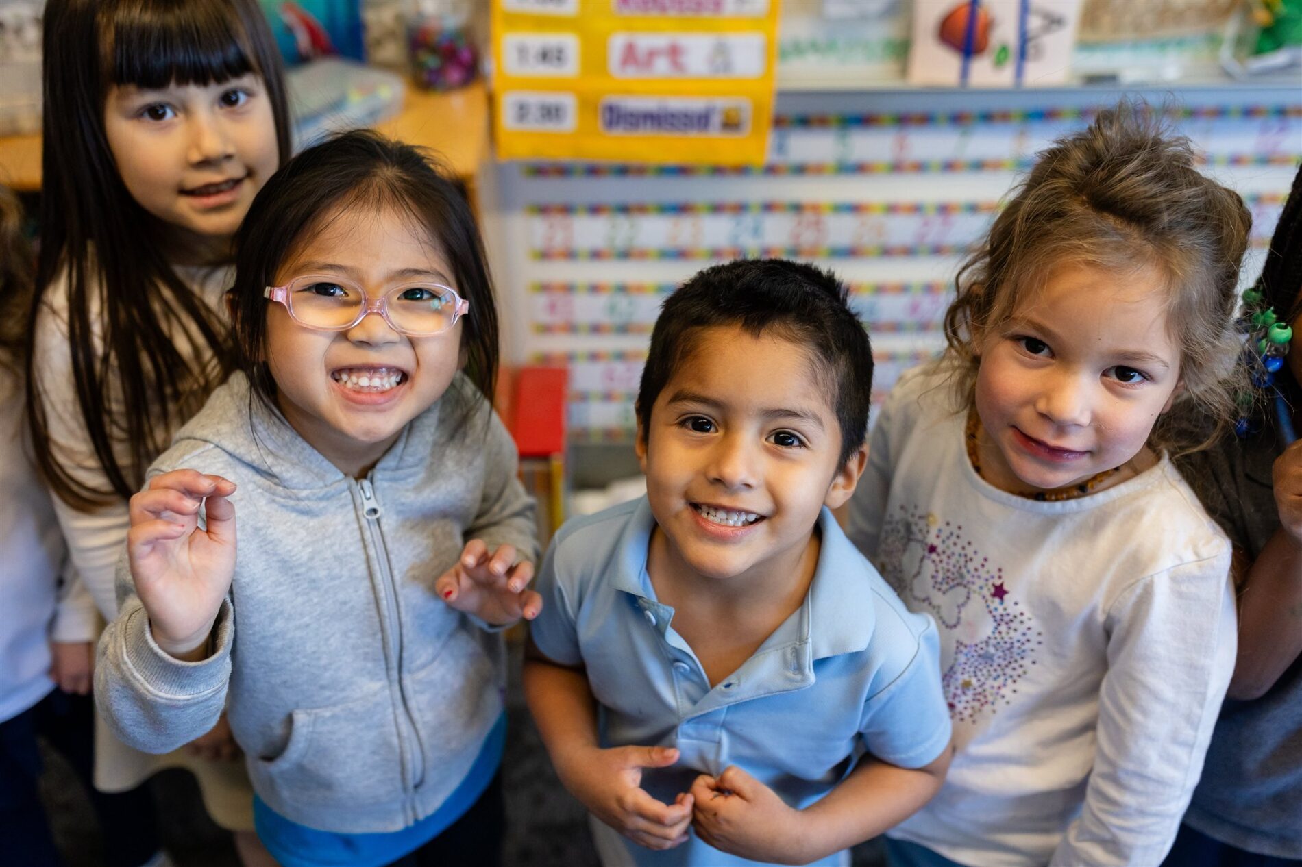 Four smiley Kavod students stand together in their classroom looking up at the camera.