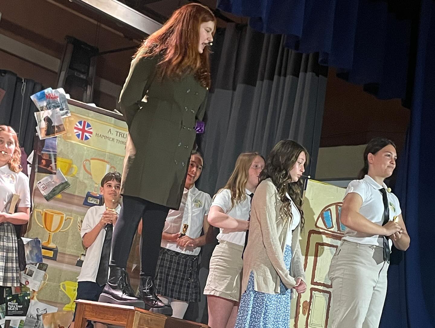 Kavod middle schoolers on stage performing the play Matilda, with the actress who plays Ms. Trunchbell standing tall atop a table