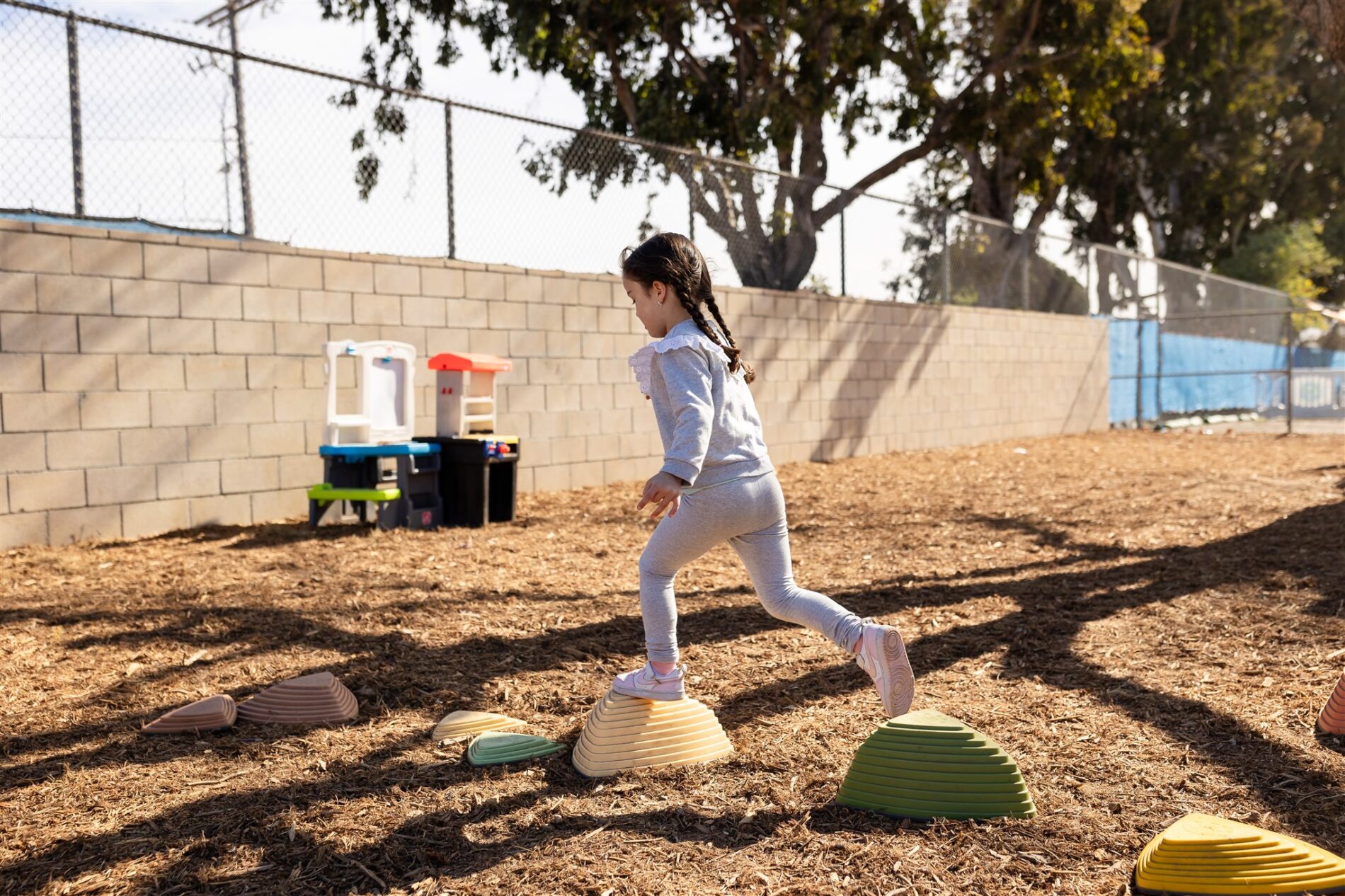 A Kavod kindergartener balancing on stepping stones walking from one stone to the next, while outside during recess.