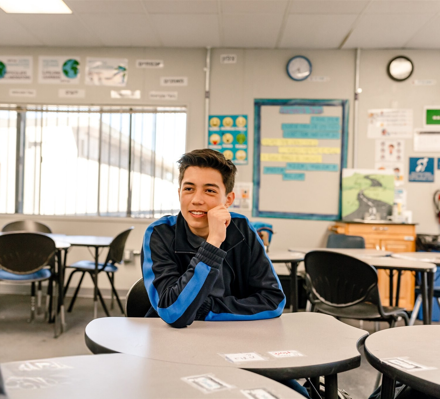 Kavod student sits at desk in classroom chatting with a classmate.
