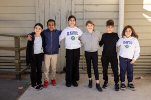 Kavod students stand next to each other outside while smiling at the camera.