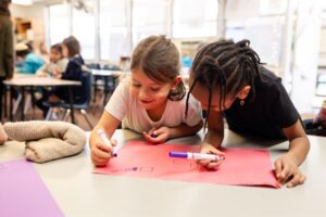 Two Kavod students holding markers while working together on a poster.

