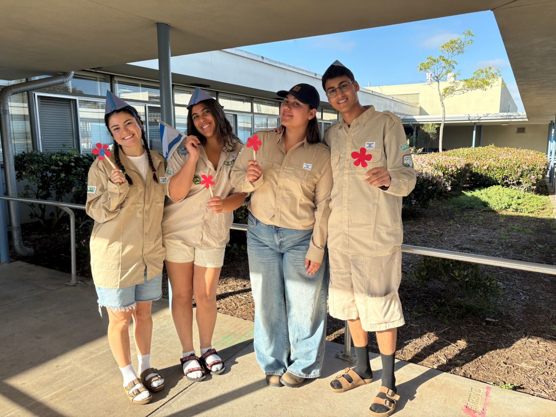 From left to right – the 4 new Shin-Shinims at Kavod: Ori, Libi, Adva, and Alon outside holding flowers and a mini Israeli flag.