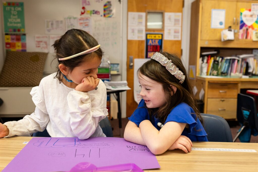 Two Kavod Charter School students sit at their desks with a purple piece of construction paper in front of them.
