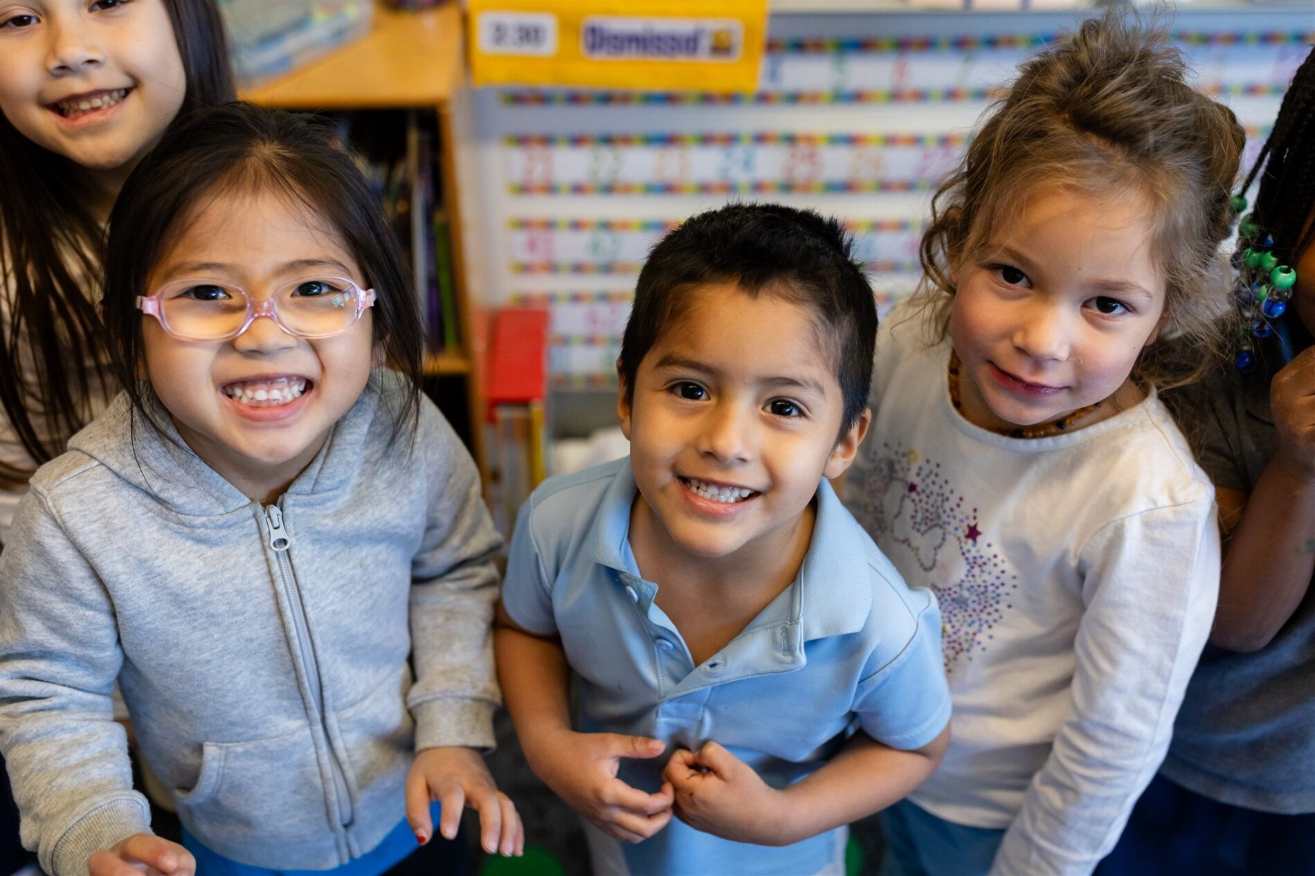 Kavod Charter School students stand next to each other in their classroom and smile for the camera.