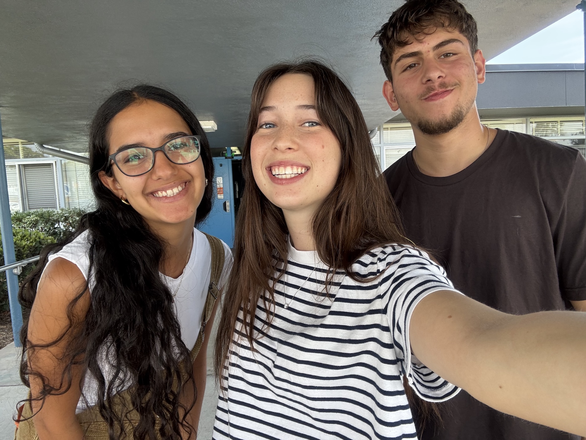 Kavod's three Shinshinim stand together for a group selfie, smiling at the camera